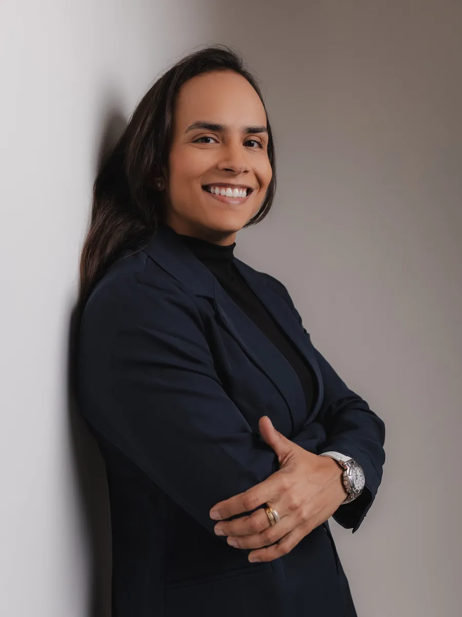 Dra. Camila Abreu sorrindo, de blazer azul marinho e braços cruzados